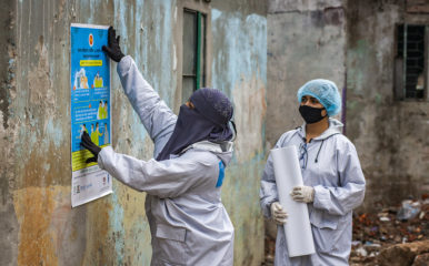 women in protective clothing putting up public health notices on a wall