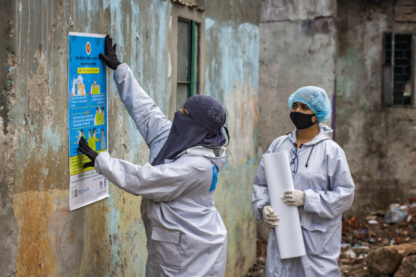 women in protective clothing putting up public health notices on a wall