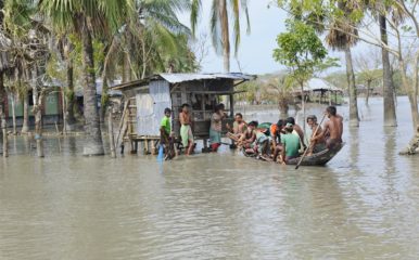 People on boat at shop on stilts in flood, Bangladesh