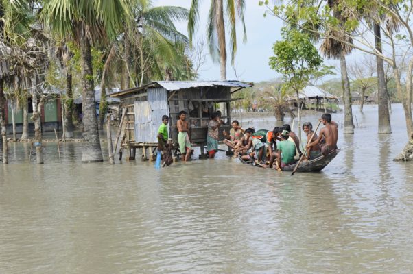 People on boat at shop on stilts in flood, Bangladesh