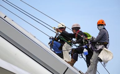 three peple climbing on ropes up a slope
