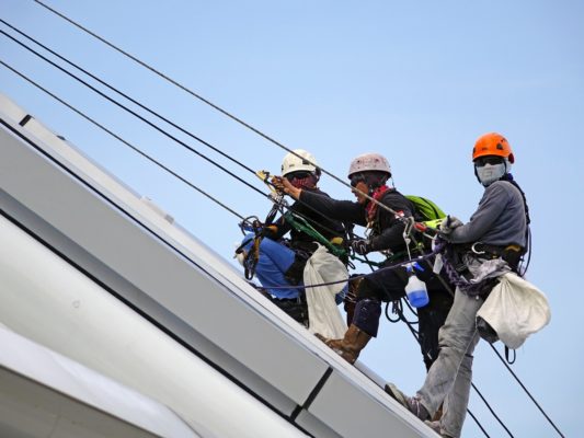 three peple climbing on ropes up a slope