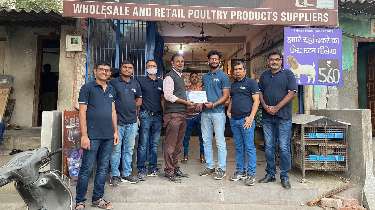 researchers shpown lined up and presening a certificate to a shop owner outside a shop