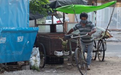 man in facemask pushing a bicycle next to a street stall.