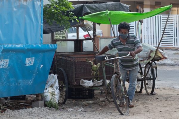 man in facemask pushing a bicycle next to a street stall.