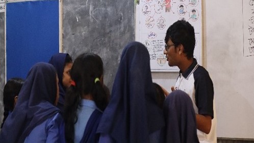 man at whiteboard surrounded by girls in hijab