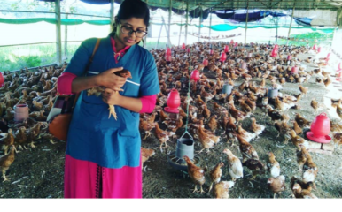 woman holding chicken and standing in a barn housing many chickens