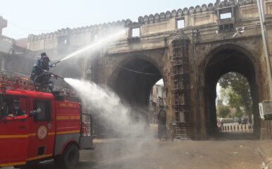 firemen on top of a fire tender spray water at a large gateway on a road