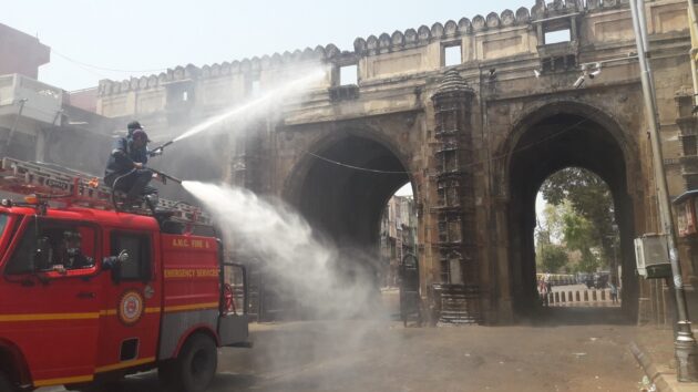 firemen on top of a fire tender spray water at a large gateway on a road